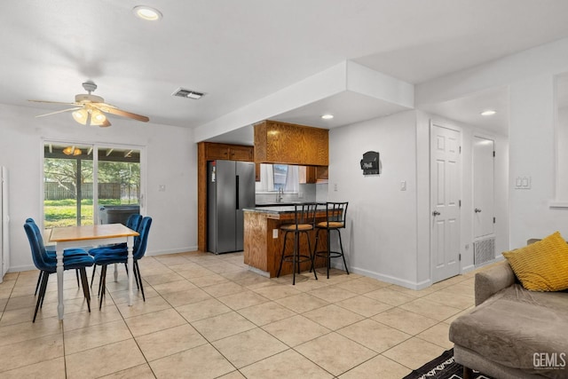 kitchen with brown cabinetry, visible vents, baseboards, freestanding refrigerator, and a peninsula