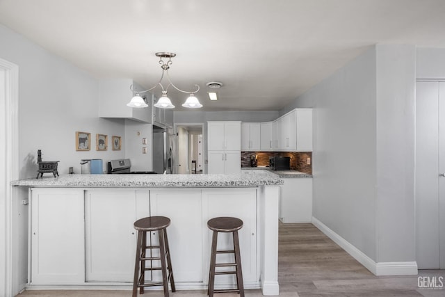 2104 B St, Bakersfield, CA 93301 - kitchen featuring a peninsula, white cabinets, stainless steel appliances, light wood-type flooring, and a kitchen bar