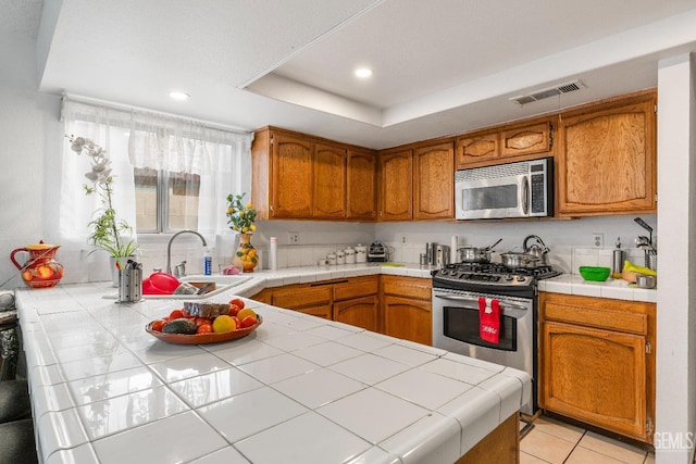 kitchen featuring tile counters, sink, stainless steel appliances, and a tray ceiling