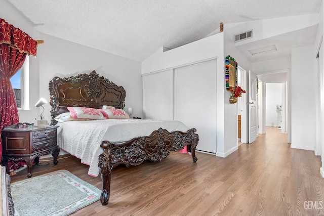 bedroom with a textured ceiling, light hardwood / wood-style flooring, a closet, and lofted ceiling