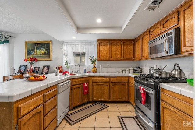 kitchen with tile countertops, a raised ceiling, sink, appliances with stainless steel finishes, and light tile patterned flooring