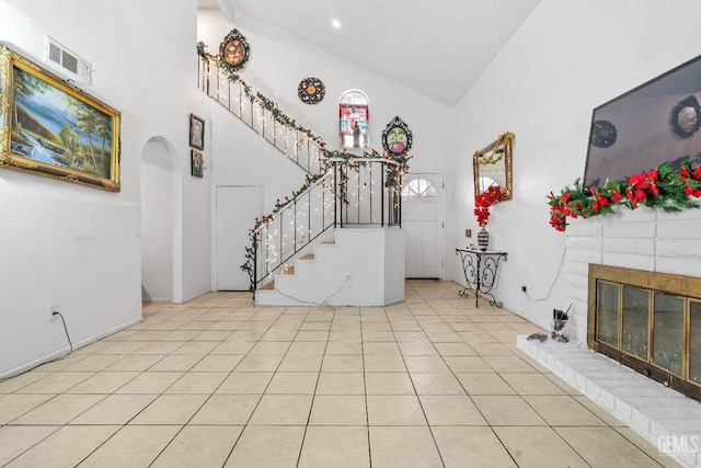 entrance foyer with light tile patterned floors, a textured ceiling, high vaulted ceiling, and a brick fireplace