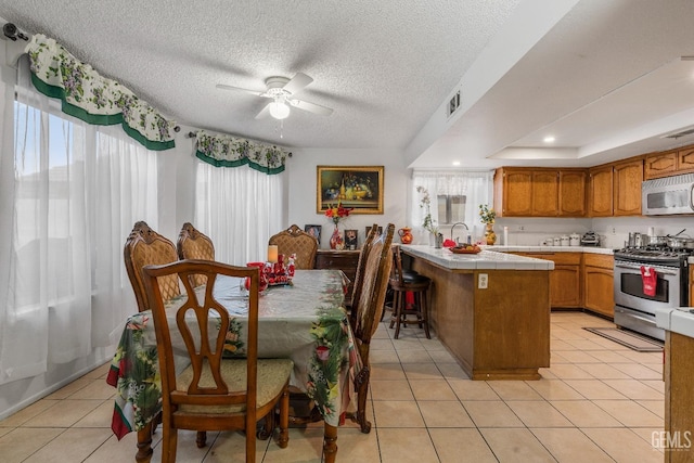 tiled dining area featuring a tray ceiling, ceiling fan, sink, and a textured ceiling