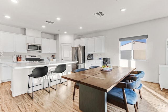 kitchen featuring white cabinetry, appliances with stainless steel finishes, a breakfast bar, and a center island with sink