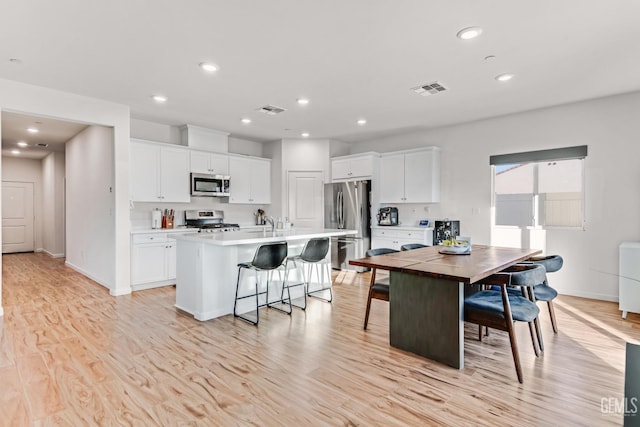 kitchen with a kitchen island with sink, light hardwood / wood-style floors, white cabinets, and appliances with stainless steel finishes