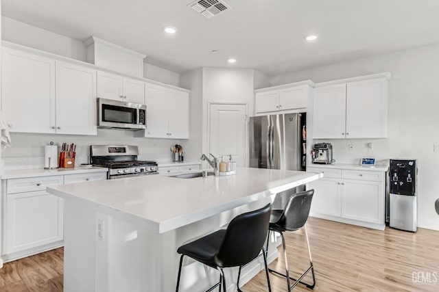 kitchen with sink, light hardwood / wood-style flooring, stainless steel appliances, a kitchen island with sink, and white cabinets