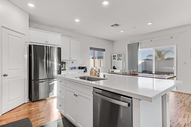 kitchen featuring appliances with stainless steel finishes, light hardwood / wood-style floors, a center island with sink, and white cabinets