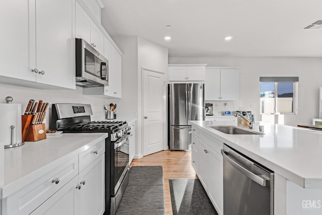 kitchen featuring stainless steel appliances, white cabinetry, sink, and a center island with sink