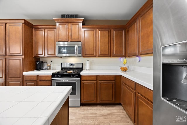 9318 Poseidon St, Bakersfield, CA 93306 - kitchen with appliances with stainless steel finishes, tile counters, light wood finished floors, and brown cabinets