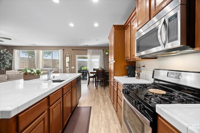 9318 Poseidon St, Bakersfield, CA 93306 - kitchen featuring stainless steel appliances, tile counters, light wood-style floors, brown cabinets, and open floor plan
