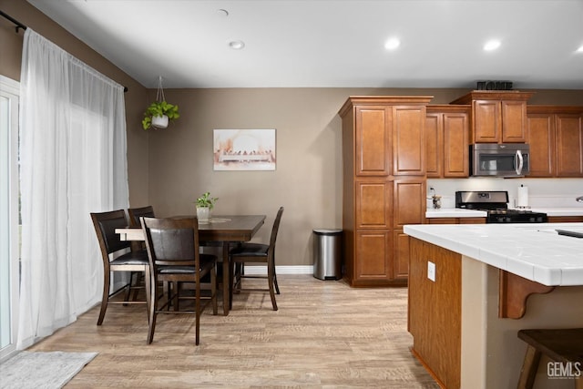 9318 Poseidon St, Bakersfield, CA 93306 - kitchen featuring stainless steel microwave, gas range, tile counters, brown cabinets, and light wood-style flooring