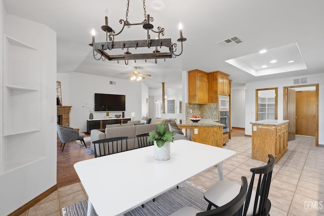 631 Faversham Way, Bakersfield, CA 93311 - dining area featuring a raised ceiling, light tile patterned floors, a ceiling fan, a fireplace, and a chandelier