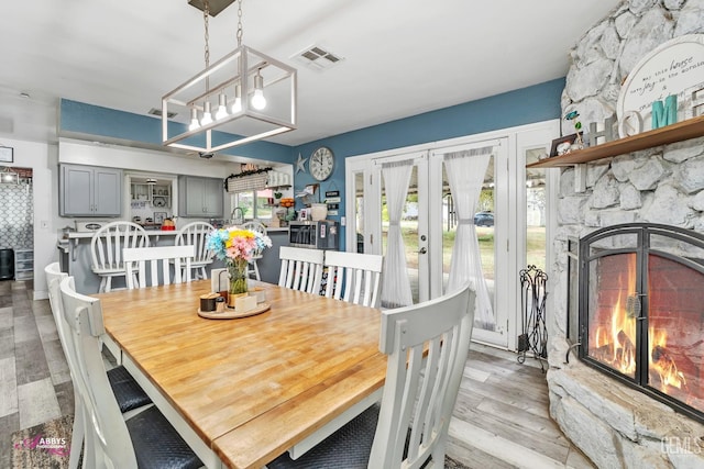 dining area with visible vents, light wood-style floors, a fireplace, and french doors