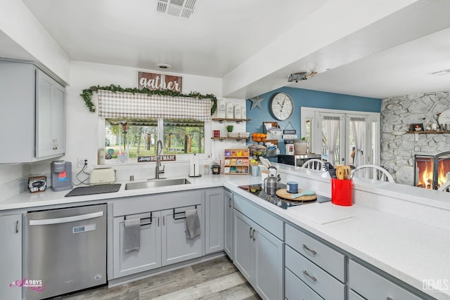 kitchen featuring stainless steel dishwasher, gray cabinets, a sink, and light countertops