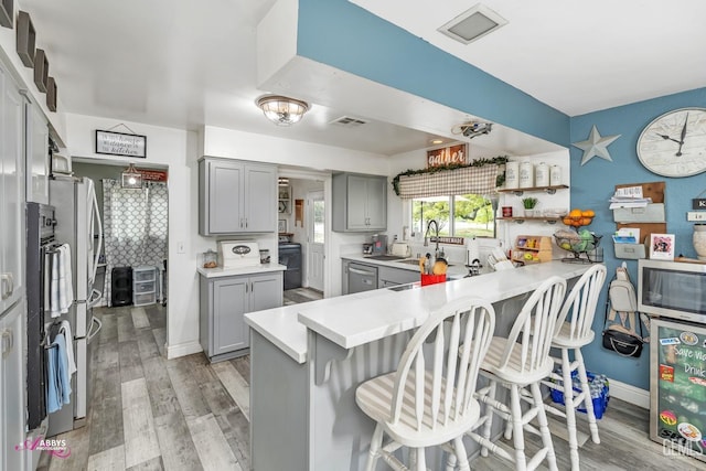 kitchen with a breakfast bar area, a peninsula, gray cabinetry, and stainless steel appliances