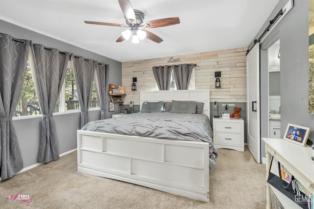 carpeted bedroom featuring wood walls, an accent wall, baseboards, a barn door, and a ceiling fan