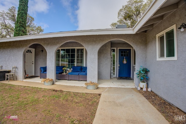 view of exterior entry with covered porch, outdoor lounge area, and stucco siding