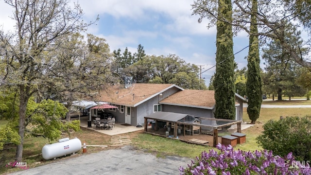 back of property with a shingled roof, stucco siding, a patio area, and a deck