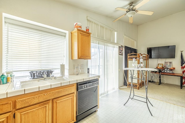 kitchen with black dishwasher, light floors, tile counters, a ceiling fan, and a sink