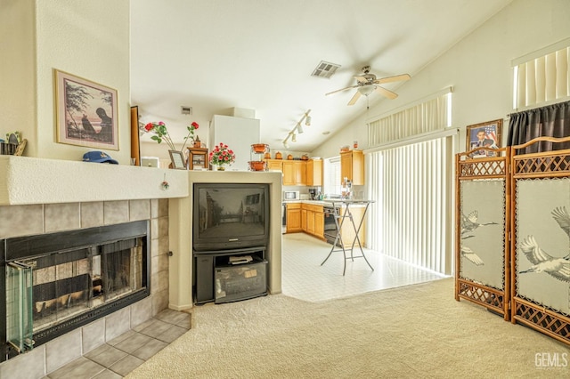 living room with light colored carpet, visible vents, vaulted ceiling, ceiling fan, and a tile fireplace