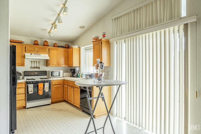 kitchen featuring lofted ceiling, white microwave, under cabinet range hood, freestanding refrigerator, and gas range oven