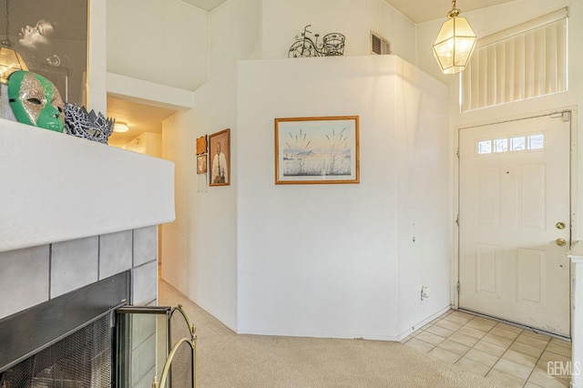 foyer entrance featuring light tile patterned floors, visible vents, a towering ceiling, light carpet, and a tile fireplace