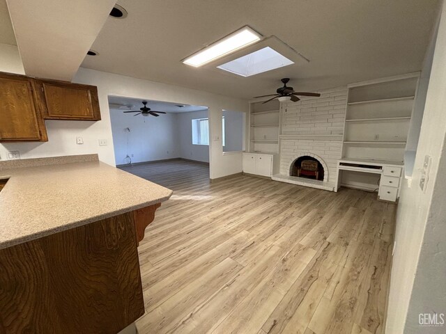 unfurnished living room with a skylight, built in features, a fireplace, and light hardwood / wood-style floors