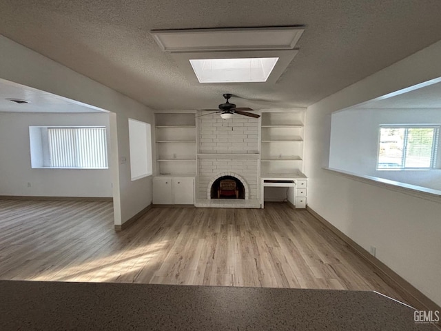 unfurnished living room with built in shelves, a brick fireplace, a skylight, and a textured ceiling