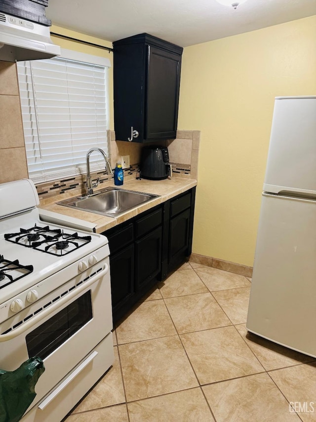 kitchen with light countertops, backsplash, light tile patterned flooring, a sink, and white appliances