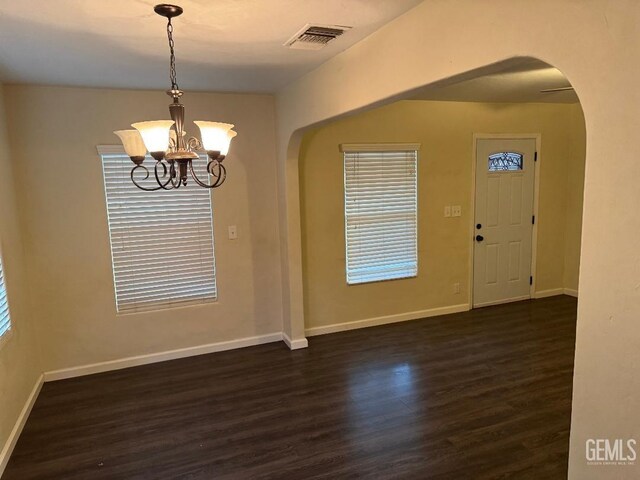 interior space featuring arched walkways, dark wood-style flooring, visible vents, baseboards, and an inviting chandelier