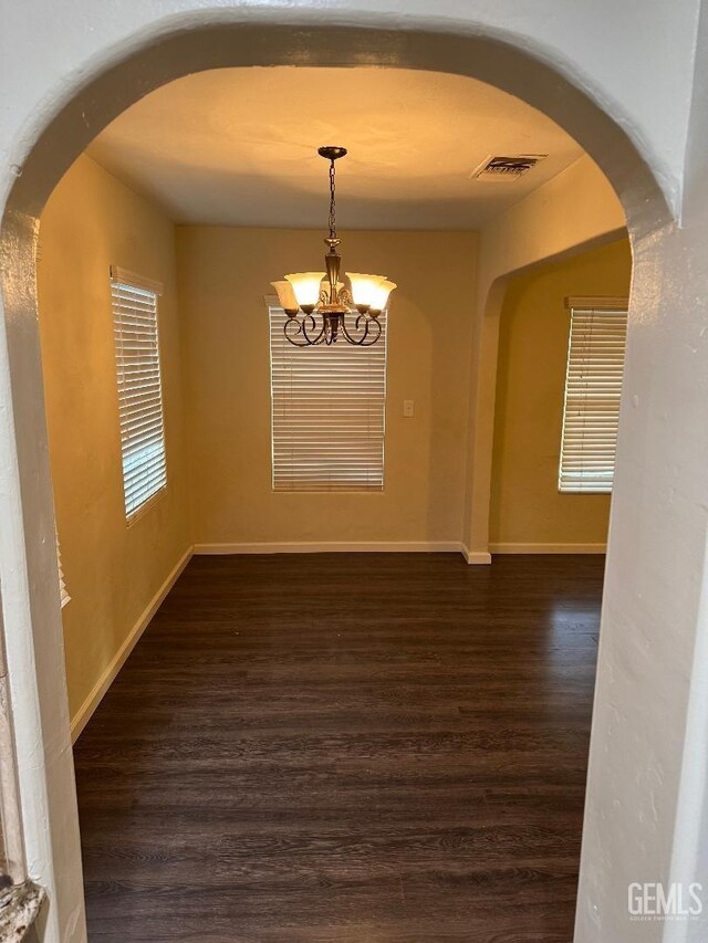 spare room with arched walkways, dark wood-type flooring, visible vents, and an inviting chandelier