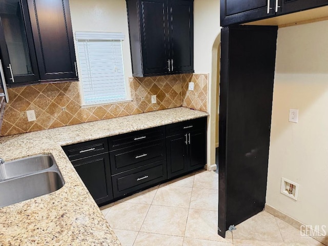 kitchen with dark cabinetry, light tile patterned flooring, a sink, and light stone countertops