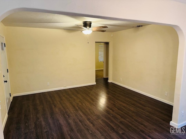 unfurnished room with baseboards, arched walkways, and dark wood-type flooring