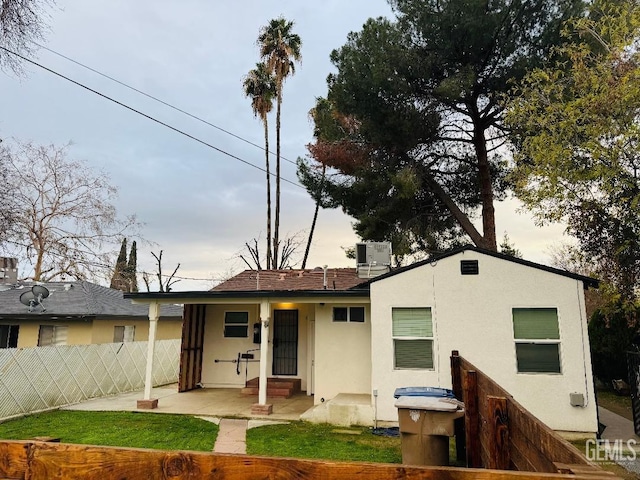 back of house at dusk with a patio, a chimney, fence, central AC, and stucco siding