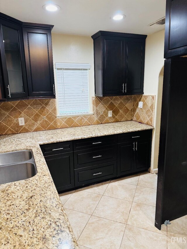 kitchen with visible vents, decorative backsplash, light stone counters, dark cabinetry, and light tile patterned flooring