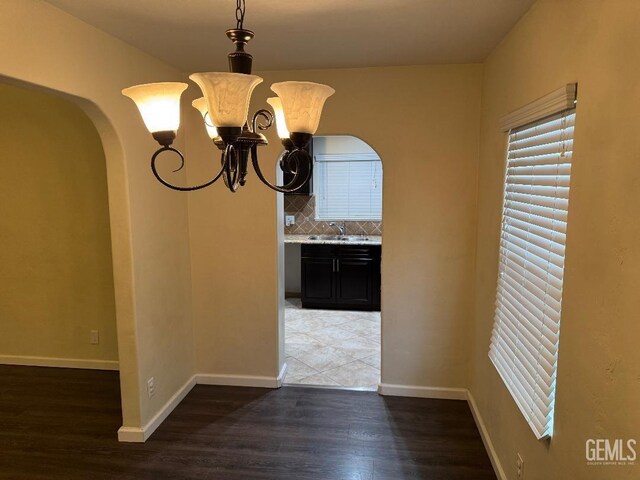 unfurnished dining area featuring baseboards, arched walkways, dark wood-style flooring, and a sink