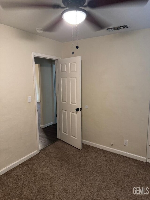 empty room featuring visible vents, dark carpet, baseboards, and ceiling fan