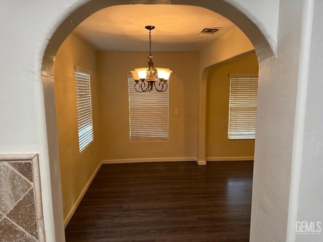 unfurnished dining area featuring arched walkways, dark wood-style flooring, a notable chandelier, visible vents, and baseboards