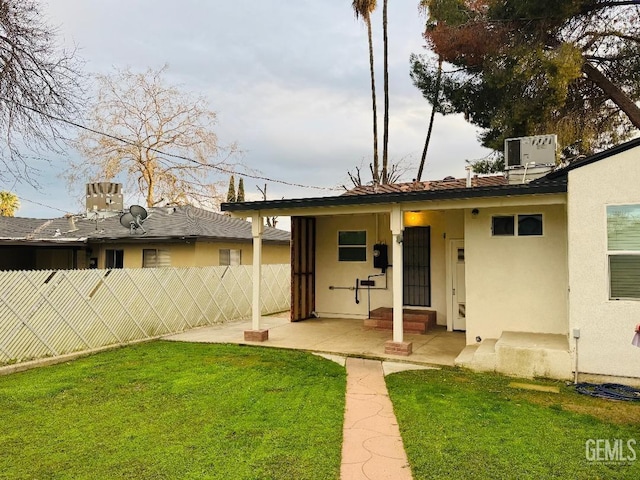 rear view of house featuring entry steps, a patio, fence, a yard, and stucco siding