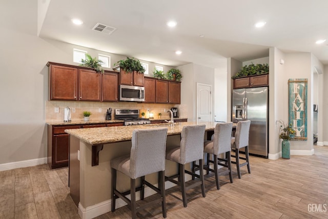 6207 Provincetown Ave, Bakersfield, CA 93313 - kitchen with stainless steel appliances, light wood-style flooring, decorative backsplash, a kitchen island with sink, and a kitchen bar