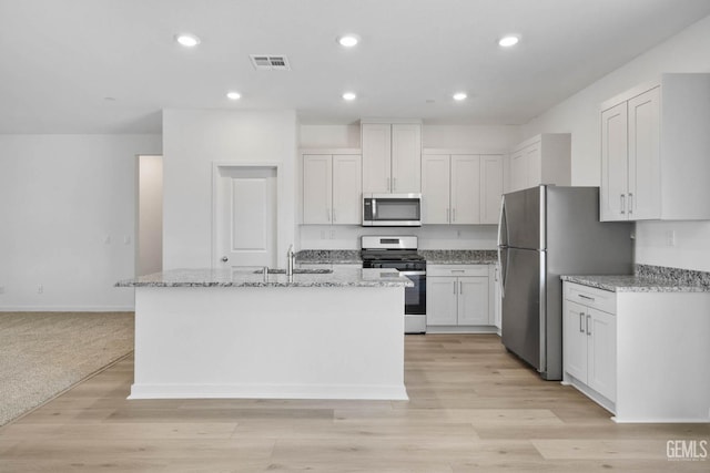 kitchen featuring light stone counters, white cabinets, a sink, appliances with stainless steel finishes, and a kitchen island with sink