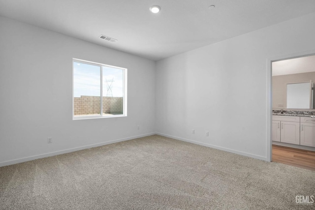 spare room featuring light colored carpet, visible vents, a sink, and baseboards