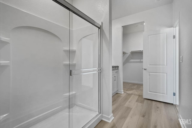 full bath with a stall shower, a walk in closet, wood finished floors, and baseboards