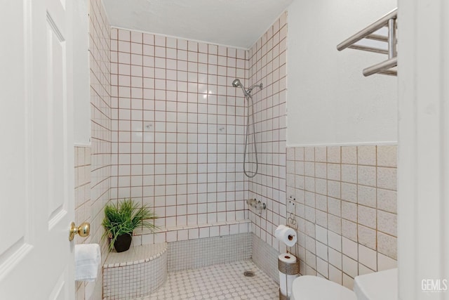 bathroom featuring toilet, tile patterned flooring, tile walls, and tiled shower