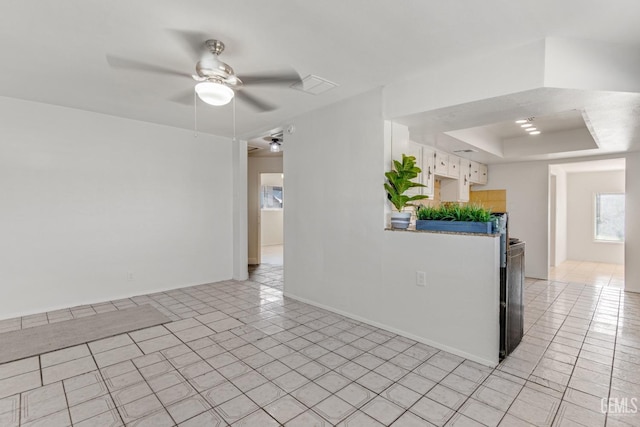 empty room with ceiling fan, light tile patterned flooring, and a tray ceiling