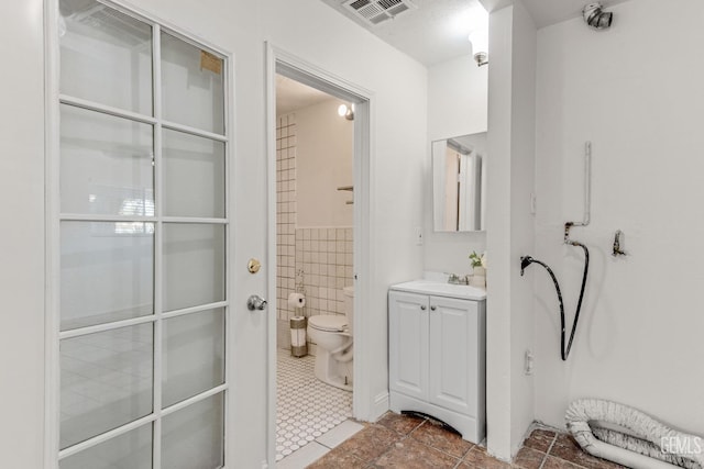 bathroom with tile patterned flooring, vanity, toilet, and tile walls