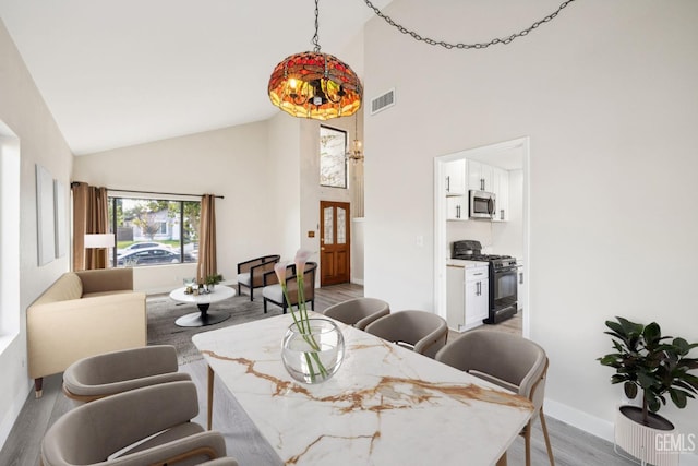 dining area with high vaulted ceiling and light hardwood / wood-style floors