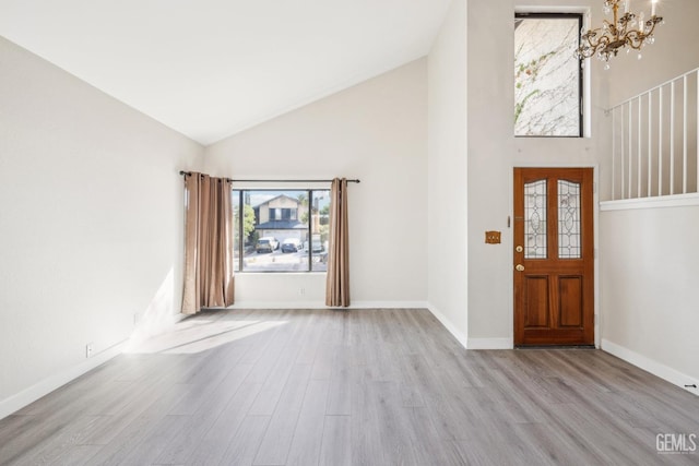 foyer entrance with high vaulted ceiling, a chandelier, and light wood-type flooring