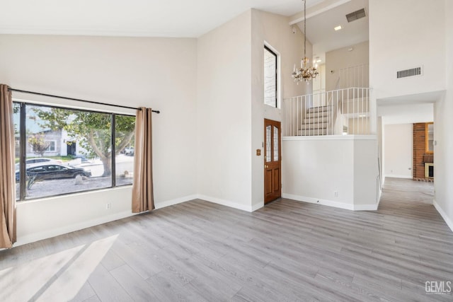 unfurnished living room with beam ceiling, a brick fireplace, an inviting chandelier, high vaulted ceiling, and wood-type flooring