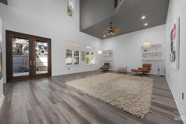 living area featuring baseboards, a towering ceiling, wood finished floors, and a ceiling fan